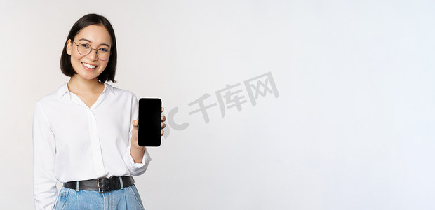 微笑的韩国女性展示智能手机屏幕，展示移动应用程序，站在白色背景上