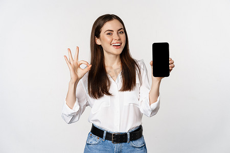 笑得开心的女人，脸上满意，推荐优秀的应用程序，显示手机屏幕，好的标志，站在白色背景上