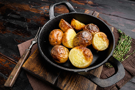 咸蹄笋干小土豆摄影照片_烤箱烤土豆配迷迭香，在煎铸铁锅中，在旧的深色木桌背景上