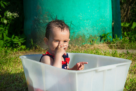 独立浴缸摄影照片_穿着泳衣的小女孩坐在浴缸里玩耍和微笑