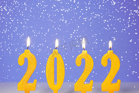 燃烧黄色蜡烛的节日背景 2022 年新年快乐概念 燃烧黄色和金色的 2022 年蜡烛在紫色背景上与飘落的雪隔离。