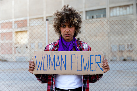 自信的非裔美国人示威抗议者看着拿着女性权力标志的相机。
