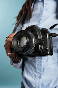 站在蓝色背景上手持现代相机设备的年轻成人摄影爱好者的特写。
