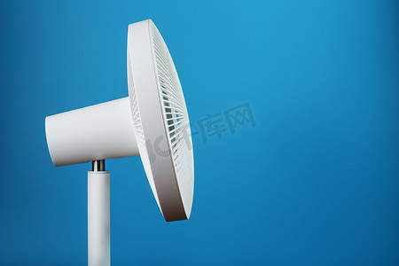 蓝色电风扇摄影照片_白色电风扇，采用现代设计，用于在蓝色背景下冷却房间