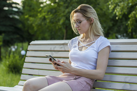 女子学习摄影照片_坐在长凳上的戴眼镜的年轻女子使用智能手机