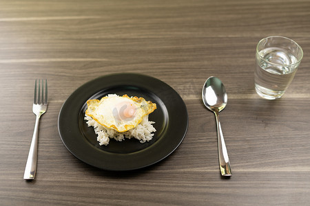 黑白米饭摄影照片_黑盘上的白米饭上煎鸡蛋，加 1 杯水、