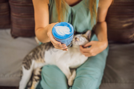 沙发猫摄影照片_年轻女子坐在沙发上享用地中海早餐，和她的猫一起喝着时髦的饮料：蓝拿铁。