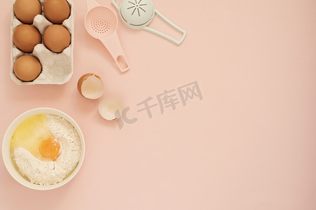 用于烹饪蛋糕或糖果的配料和厨房烘焙工具 — 鸡蛋、面粉，背景为柔和的粉红色。