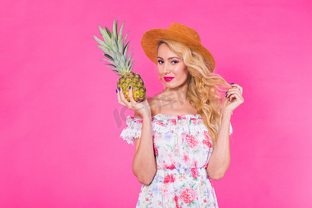 快乐的年轻女人拿着粉红色背景的菠萝。
