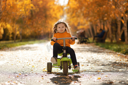 小女孩在秋季公园骑三轮自行车
