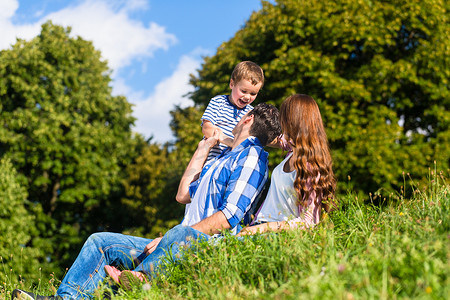孩子坐爸爸背上摄影照片_一家人坐在绿草上玩得很开心