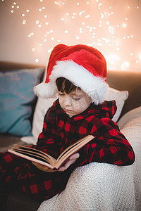 一个戴着圣诞帽的男孩正在休闲沙发上看书。