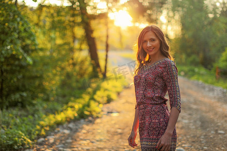 年轻女子穿着裙子，走在森林小径上，背景是金色的夕阳。