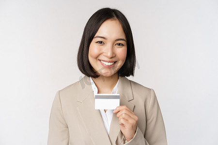 微笑的办公室文员，出示信用卡的亚洲企业女性，穿着米色西装站在白色背景上