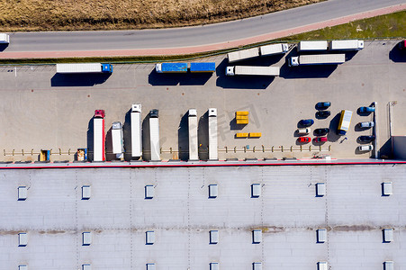 码头货运摄影照片_卡车与附加半拖车离开工业仓库/仓储大楼/装货区的空中拍摄，许多卡车正在装卸商品