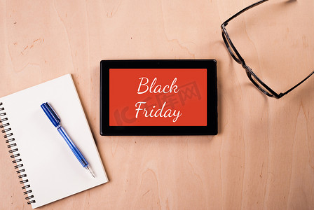 蓝色电脑框摄影照片_数字平板电脑上刻有：“黑色星期五”，主题放在木桌上：眼镜、记事本、