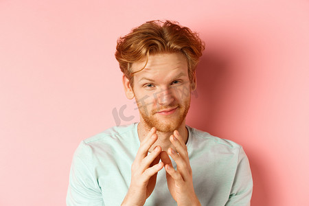 特写：留着红头发的滑稽大胡子男人制定了一个完美的计划，微笑着，尖尖的手指，策划着什么，在粉红色的背景下狡猾地站着
