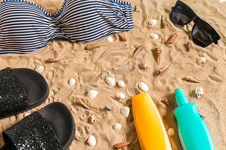 夏季比基尼和配饰时尚沙滩套装、沙滩比基尼夏季服装和海沙为背景、顶视图、概念