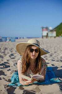 一个年轻的黑发女人在海滩上放松、阅读博文的肖像