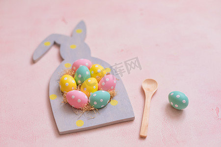粉红色混凝土背景中兔子形框架中的彩色圆点复活节彩蛋