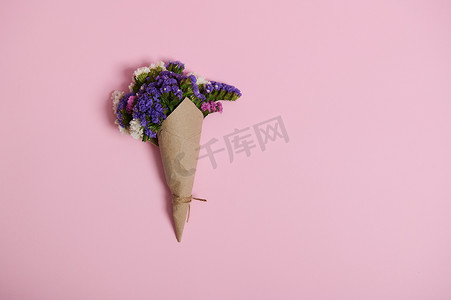 平躺的美丽草甸花的花卉组合物包裹在用绳子绑着的包装工艺纸中，在粉红色背景上与复制空间隔离。