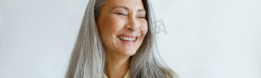 灰色背景下头发灰白、双臂交叉、面带微笑的亚洲女性肖像