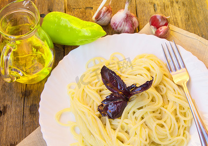 白盘里的意大利面，旧木桌上放着罗勒，玻璃罐里放着蔬菜和橄榄油