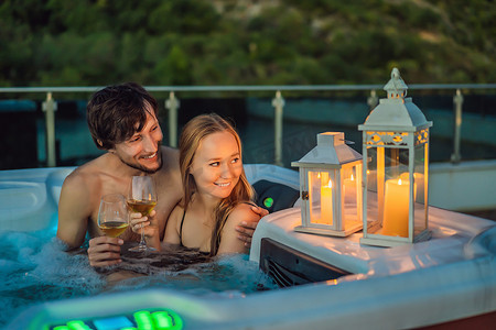 在绿色大山的背景下，享受快乐旅行时光假期生活的年轻无忧无虑的快乐微笑夫妇在热水浴缸中放松的肖像