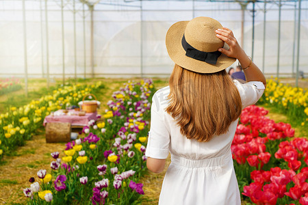 女孩拿鲜花摄影照片_美丽的女孩拿着草帽在花间行走，准备在日落时野餐。