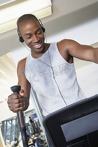 快乐的非洲裔美国人在健身房听音乐时在椭圆机上