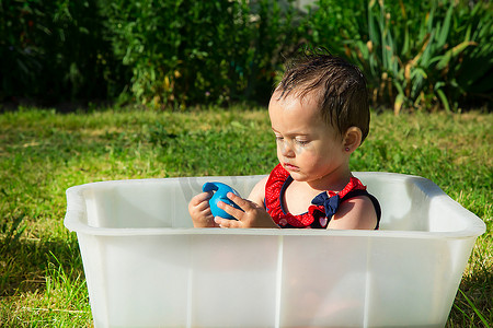 在炎热的夏日，一个非常严肃的女孩在白色的浴缸里玩蓝色的橡胶玩具