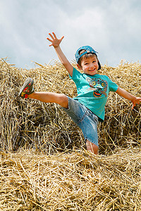 炎热摄影照片_夏日男孩在稻草捆上跳跃和玩耍