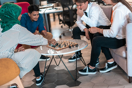 在现代创业办公室的休闲区休息时，多民族商人下棋
