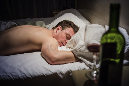 宿醉摄影照片_晚上躺在床上的宿醉男人