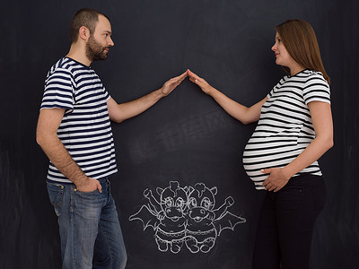 儿童的想象力摄影照片_怀孕的夫妇在粉笔板上画出他们的想象力