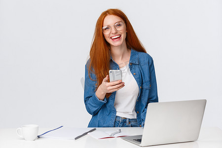 开朗、友善、魅力四射的红发女设计师，留着红色狐狸头发、戴眼镜、无忧无虑地笑着、拿着智能手机、用笔记本电脑完成项目、喝咖啡的自由职业者