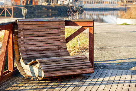 户外家具，河岸上的一把木椅，在平静光滑的水面模糊的背景下，被明亮的阳光照亮。