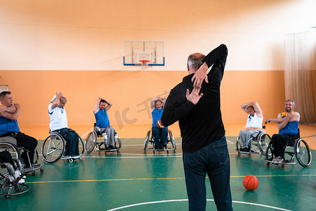 选拔摄影照片_残疾篮球队的选拔员站在球员面前，为他们展示训练开始前的伸展运动
