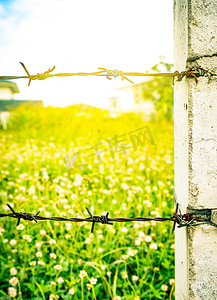生锈的旧栅栏铁丝网与混凝土杆在模糊的花田上作为背景与耀斑光。