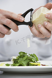 男装饰品摄影照片_一位男厨师在沙拉上磨碎奶酪的特写中段