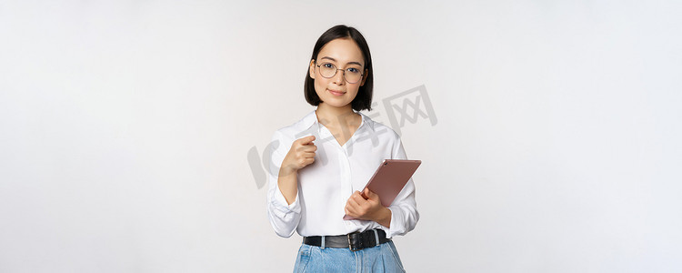 韩国女性，戴眼镜的办公室经理，拿着工作平板电脑，指着你，选择招聘，站在白色背景中