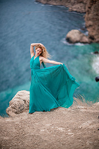 飞舞的丝绸摄影照片_身着翡翠裙的女子，长着丝绸长翅膀的时装模特，飘逸的长裙，飞舞的布料在堤岸上。
