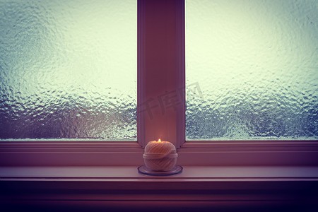 冬日暮光中燃烧的蜡烛和磨砂的窗户
