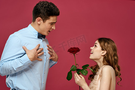 西装晚礼服摄影照片_浪漫情侣的肖像，在孤立的背景和经典的西装晚礼服上爱上了红玫瑰