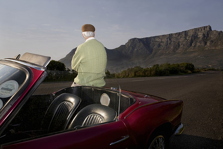 南非开普敦信号山上，老人欣赏靠在老式赛车上的景色