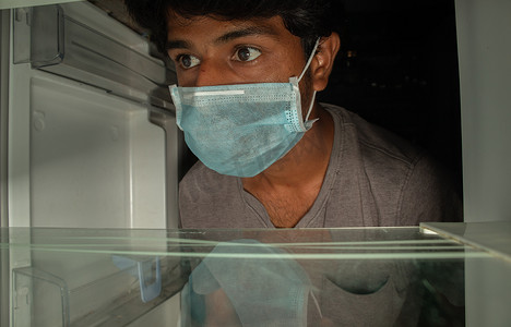 戴医用口罩的男子在空冰箱或冰箱里寻找食物 — covid-19或冠状病毒家庭隔离期间没有食品储藏室食物的概念
