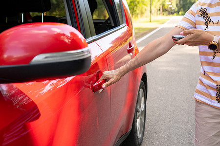 女性手按遥控汽车报警系统。女性手按遥控器上的按钮锁定或解锁红色汽车，旅行概念