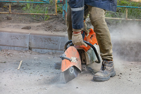 道名摄影照片_一名工人使用便携式电锯和金刚石切割盘切割道路上的旧沥青。