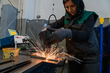 在现代金属生产和加工行业工作的一名妇女焊接产品并为数控机床做准备