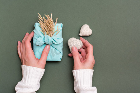 绿色背景下女性手中的情人节 furoshiki 和针织心的环保礼物